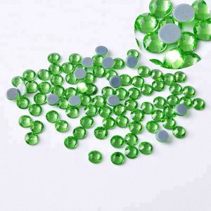 Nahaufnahme glänzender grüner (Grass Green) Hotfix Glas-Strasssteine (SS20). Zeigt Details der Facetten und den schmelzenden Kleber für Textilien. Ideal für DIY.