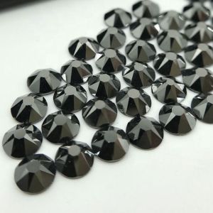 Nahaufnahme glänzender schwarzer (Jet) Hotfix Glas-Strasssteine (SS20). Zeigt Details der Facetten und den schmelzenden Kleber für Textilien. Ideal für DIY.
