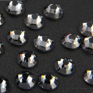 Nahaufnahme glänzender Black Diamond Hotfix Glas-Strasssteine (SS10). Zeigt Details der Facetten und den schmelzenden Kleber für Textilien. Ideal für DIY.