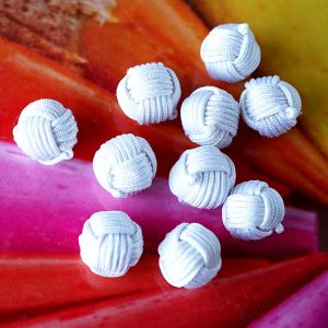 Zehn kugelförmige Knäuelknöpfe in der Farbe Weiss. Die Oberfläche aus feiner Satinkordel imitiert die Wicklung eines Wollknäuels und verleiht eine tolle Haptik.