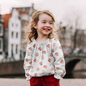 Musselin Stoff mit roten Erdbeeren auf weiss - das Bild zeigt ein N&auml;hbeispiel: kleines M&auml;dchen tr&auml;gt eine Bluse aus diesem Musselin.