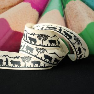 Nahaufnahme des Ripsbandes in Ecru. Das detailreiche, schwarze Scherenschnitt-Motiv eines Alpaufzuges ist gut erkennbar.