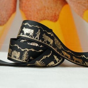 Nahaufnahme des schwarzen, matten Satinbandes. Gut erkennbares, glänzendes Alpaufzug-Motiv in Gold. Perfekt für Taschen, Accessoires und Etuis.