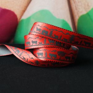 Nahaufnahme des Webbandes in rot. Das detailreiche, schwarze Scherenschnitt-Motiv eines Alpaufzuges ist gut erkennbar.